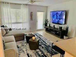 Living area featuring large windows with window treatments, neutral flooring, a ceiling fan, and a glass-paneled exterior door