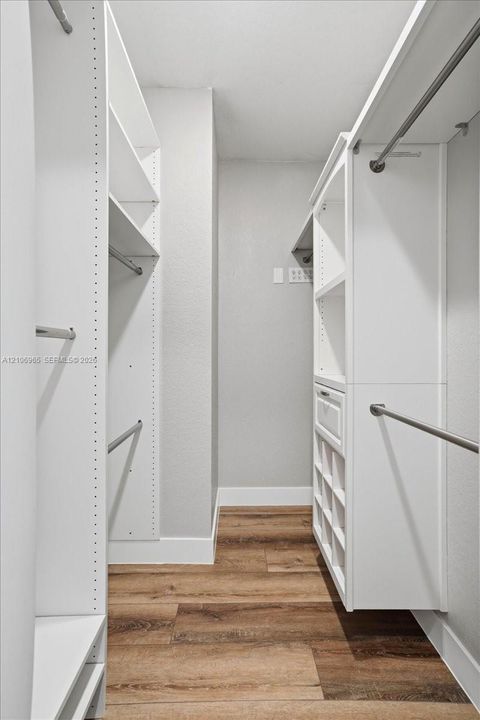 Walk-in closet featuring white built-in shelving, integrated storage drawers, chrome hanging rods, and wood-finish flooring