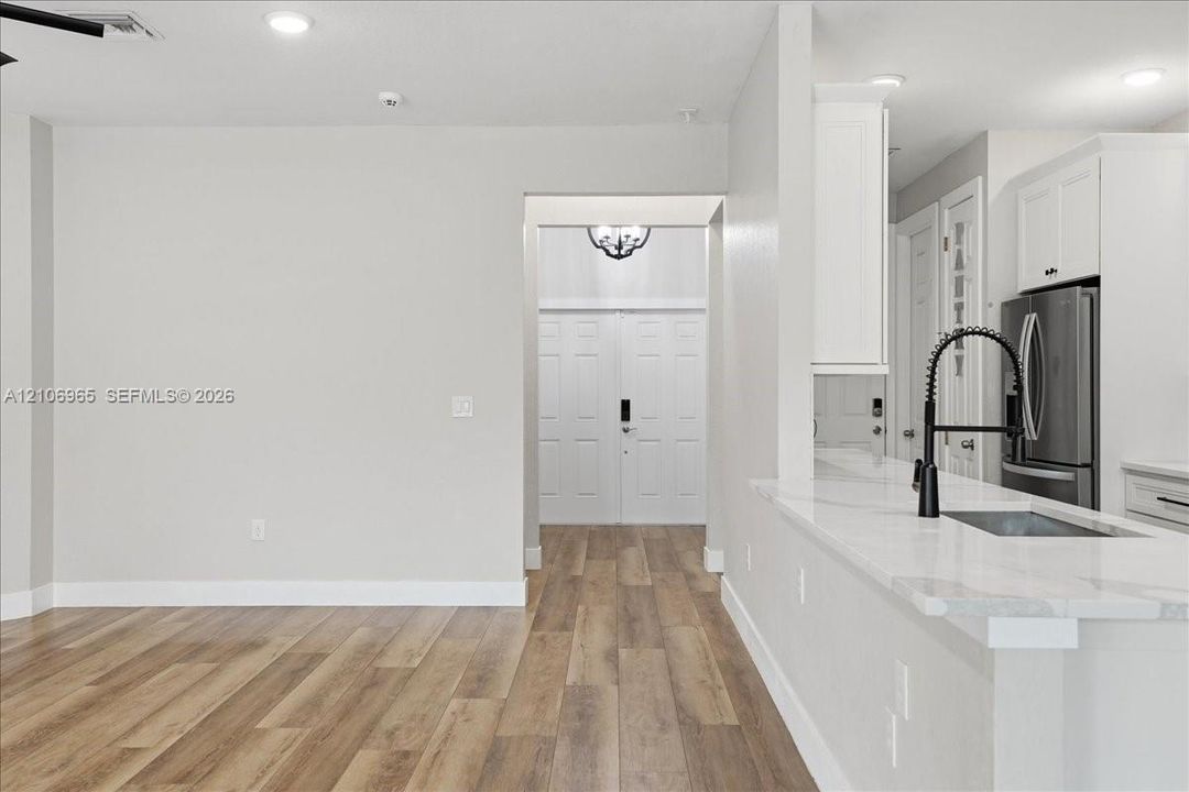Kitchen featuring a stone-surface breakfast bar, matte black gooseneck faucet, white shaker-style cabinetry, recessed lighting, and wood-finish flooring