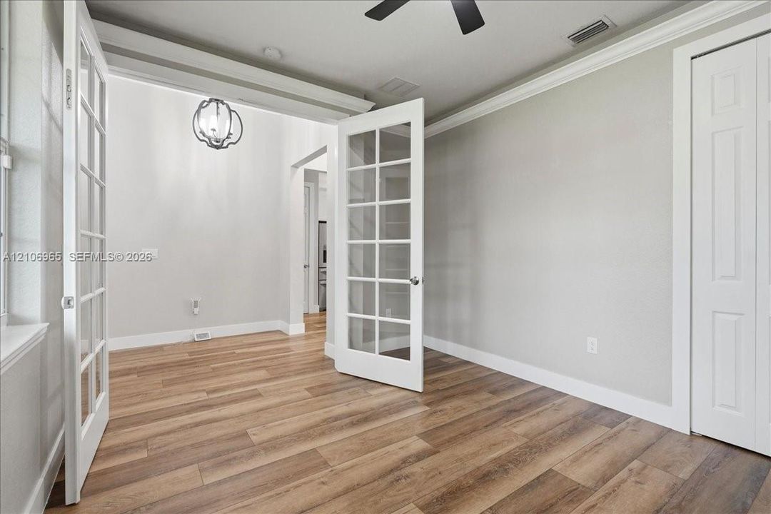 Room featuring wood-finish flooring, dual French doors with glass panes, crown molding, and a pendant light fixture
