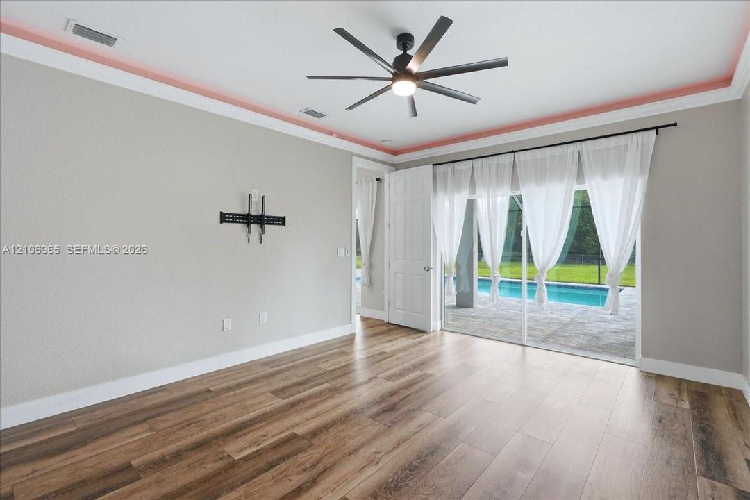 Living area featuring wood-finish flooring, recessed tray ceiling detailing, multi-blade ceiling fan, and sliding glass doors with access to an exterior screened-in pool area