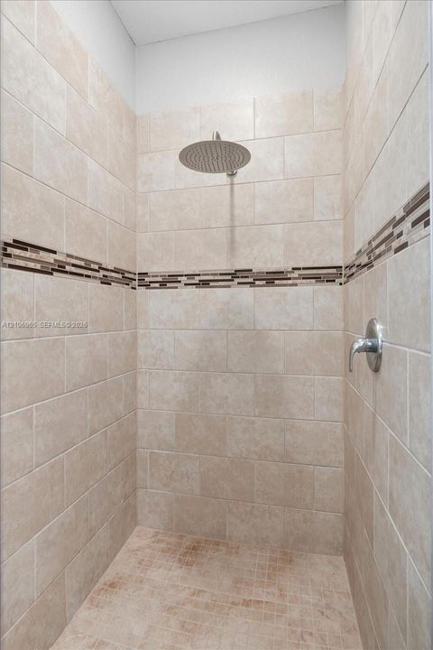 Walk-in shower featuring floor-to-ceiling neutral tile, a decorative glass mosaic accent border, a ceiling-mounted rainfall showerhead, and a wall-mounted chrome control fixture