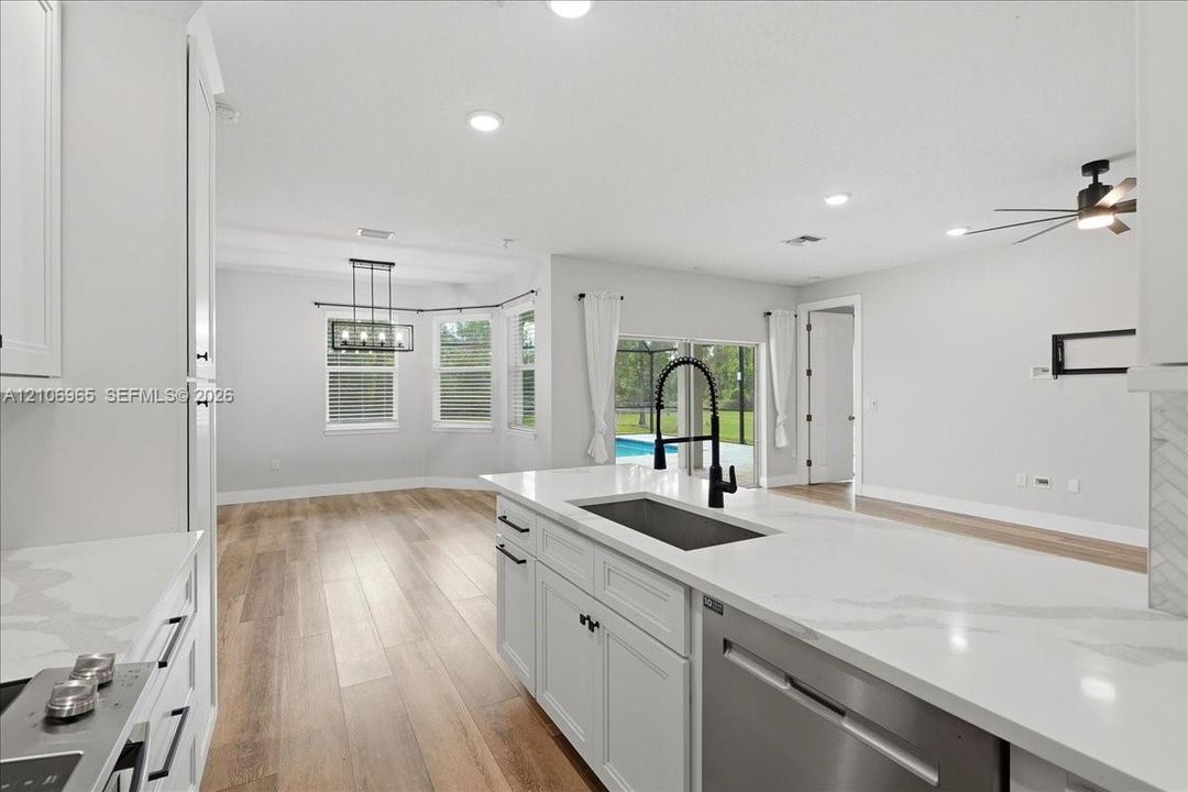 Kitchen featuring a central island with a stone-look countertop, undermount sink with a matte black high-arch faucet, white cabinetry, wood-finish flooring, and recessed ceiling lighting