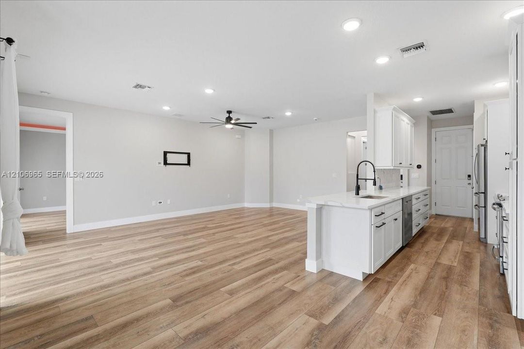 Open concept interior featuring wood-finish flooring, recessed lighting, white cabinetry, solid-surface countertops, and a kitchen island with a matte black faucet