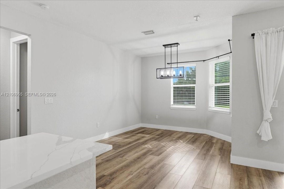 Interior space featuring wood-finish flooring, a contemporary rectangular chandelier, dual windows, and a white countertop with grey veining