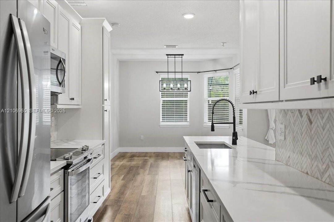 Kitchen featuring white shaker cabinetry, stone-finish countertops, herringbone-pattern backsplash, stainless steel appliances, and wood-finish flooring