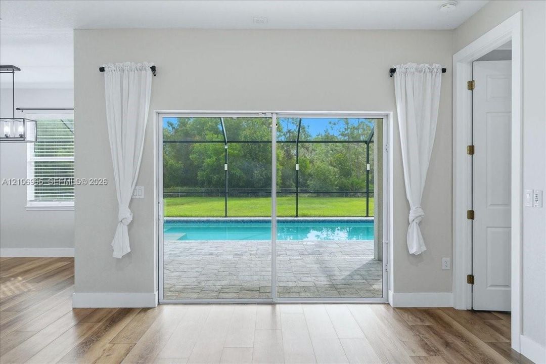 Sliding glass doors opening to a screened-in patio with a swimming pool and pavers, complemented by wood-finish flooring