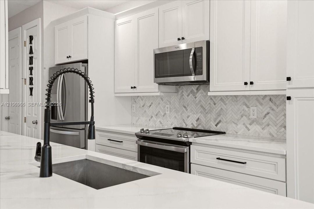 Kitchen featuring white shaker cabinetry, stainless steel appliances, herringbone-pattern stone backsplash, stone countertops, and a matte black gooseneck faucet