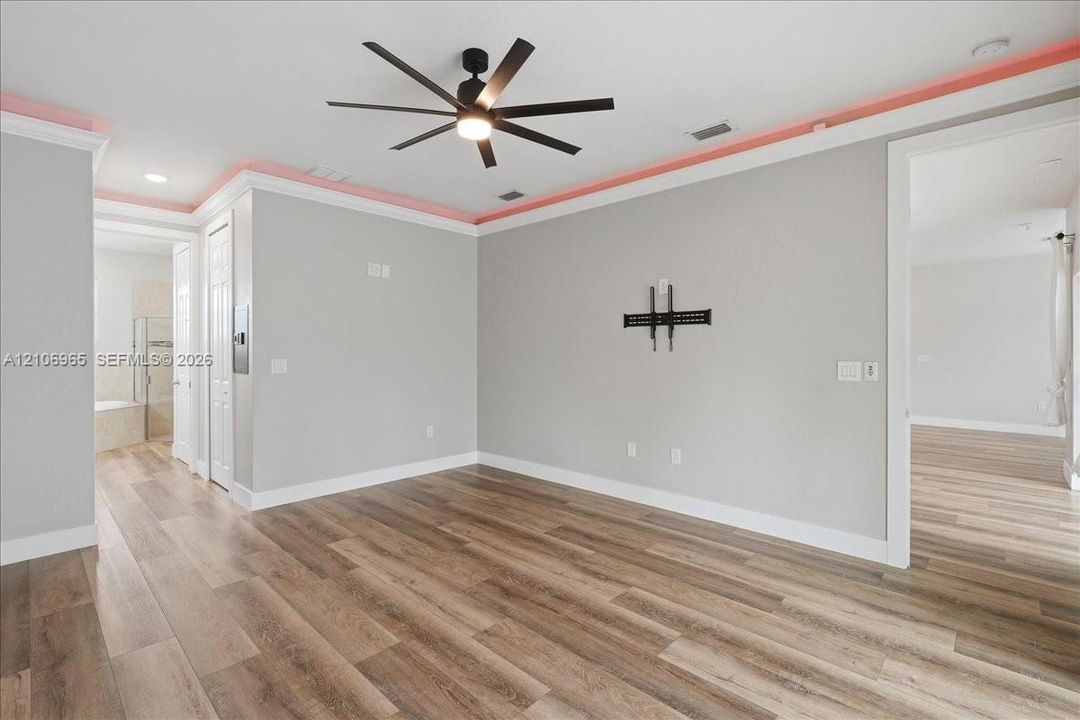 Living space featuring wood-finish flooring, recessed ceiling lighting, crown molding with accent lighting, and a multi-blade ceiling fan