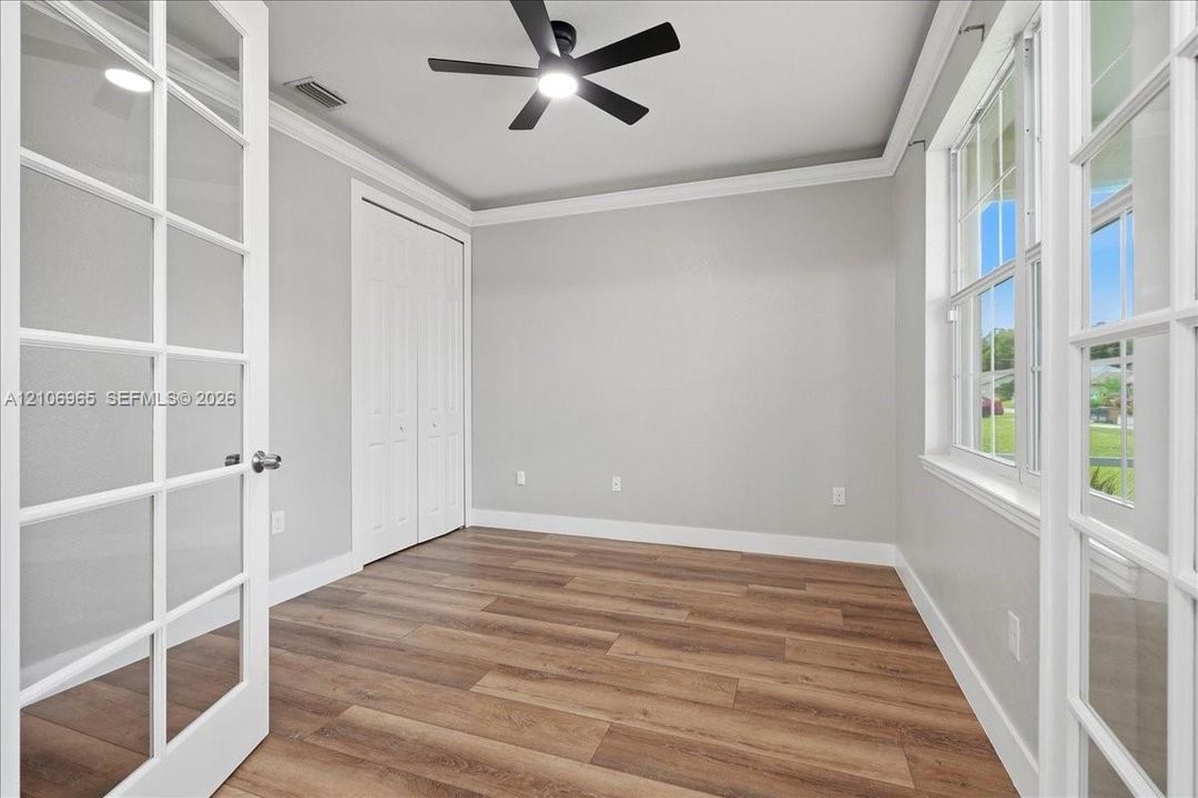 Interior space featuring wood-finish flooring, multi-pane French doors, crown molding, double-door closet, and a ceiling fan with integrated lighting