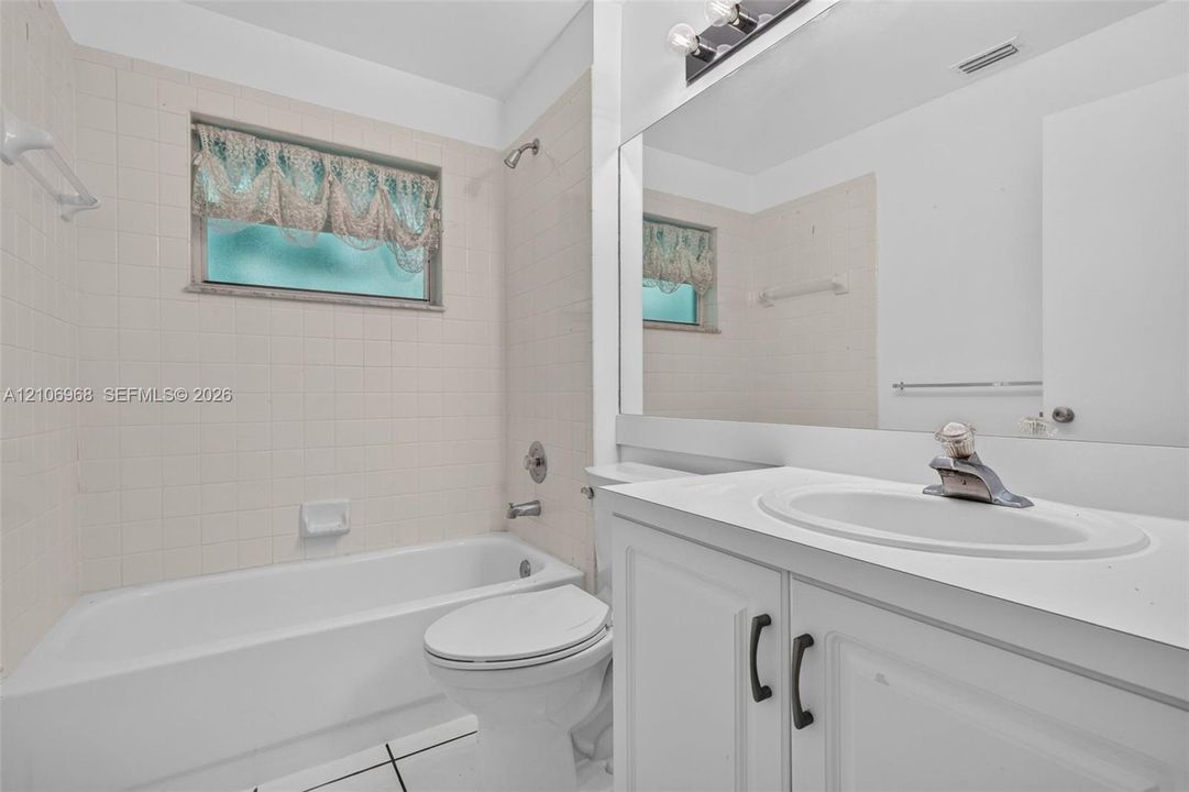 Bathroom featuring a white vanity cabinet with a solid surface countertop, an undermount sink with a chrome faucet, a large wall-mounted mirror, and a tiled shower-tub combination