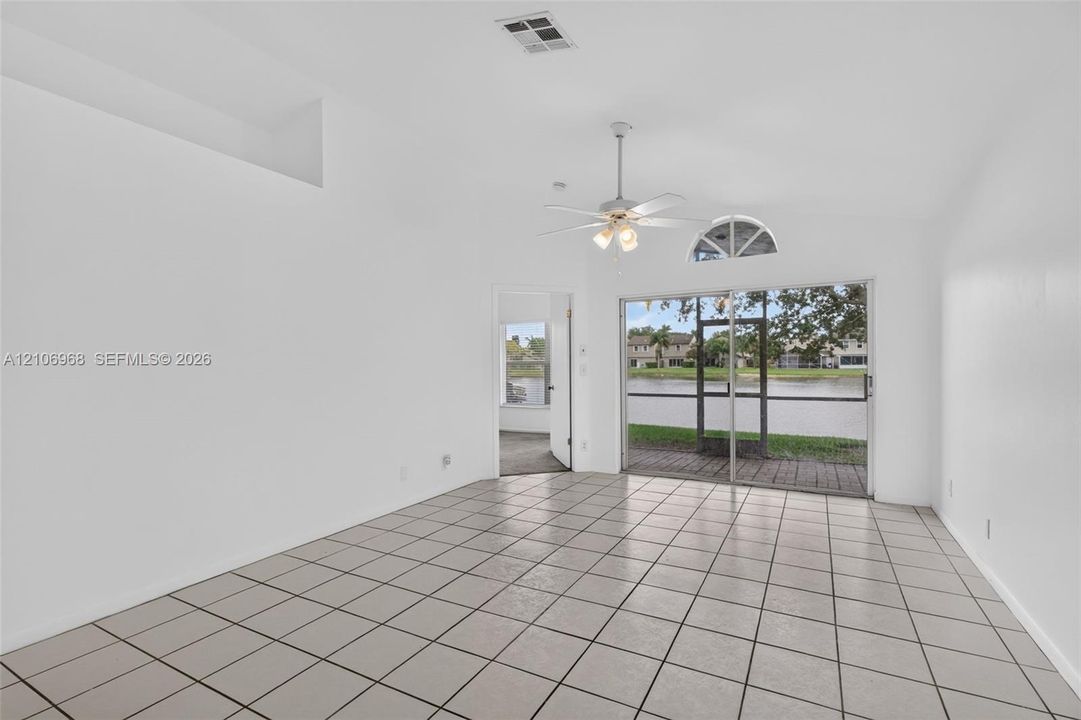 Interior space featuring vaulted ceilings, ceramic tile flooring, a multi-blade ceiling fan with integrated lighting, a decorative arched window, and sliding glass doors with exterior water access
