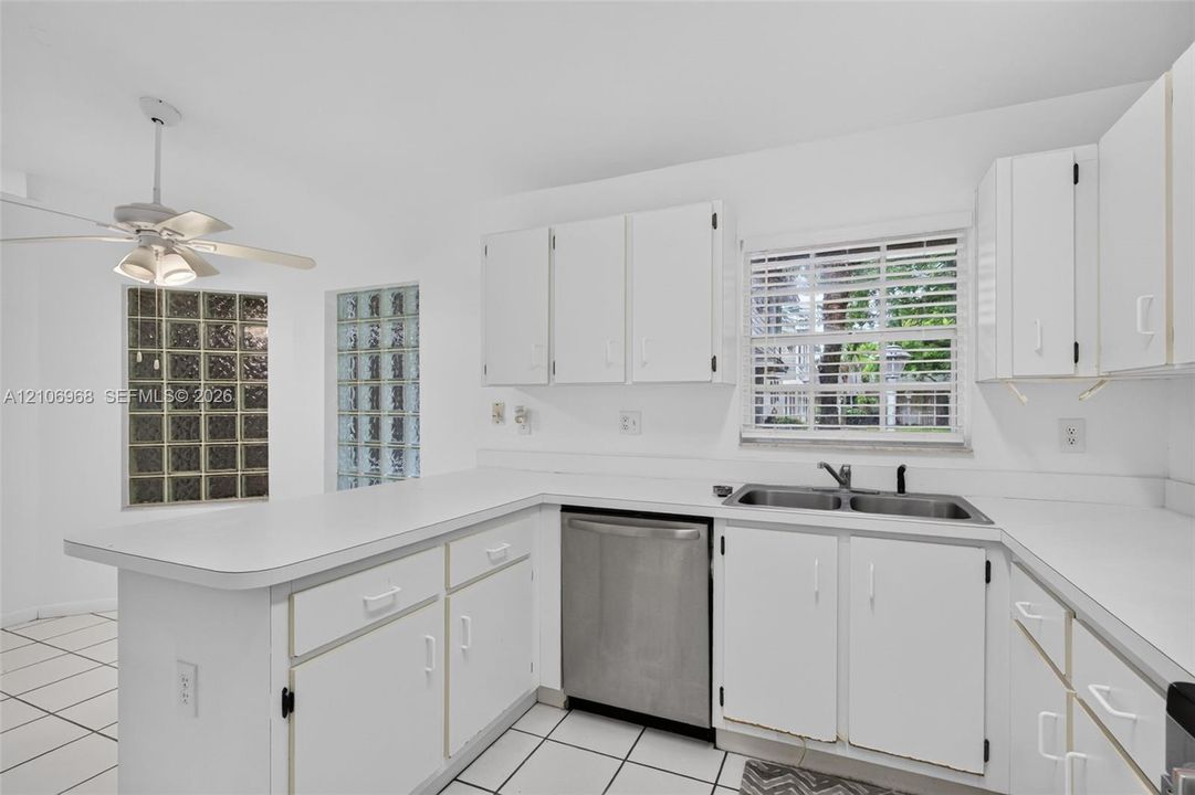 Kitchen featuring white cabinetry, a stainless steel dishwasher, glass block accents, tile flooring, and a ceiling-mounted light fixture with a fan