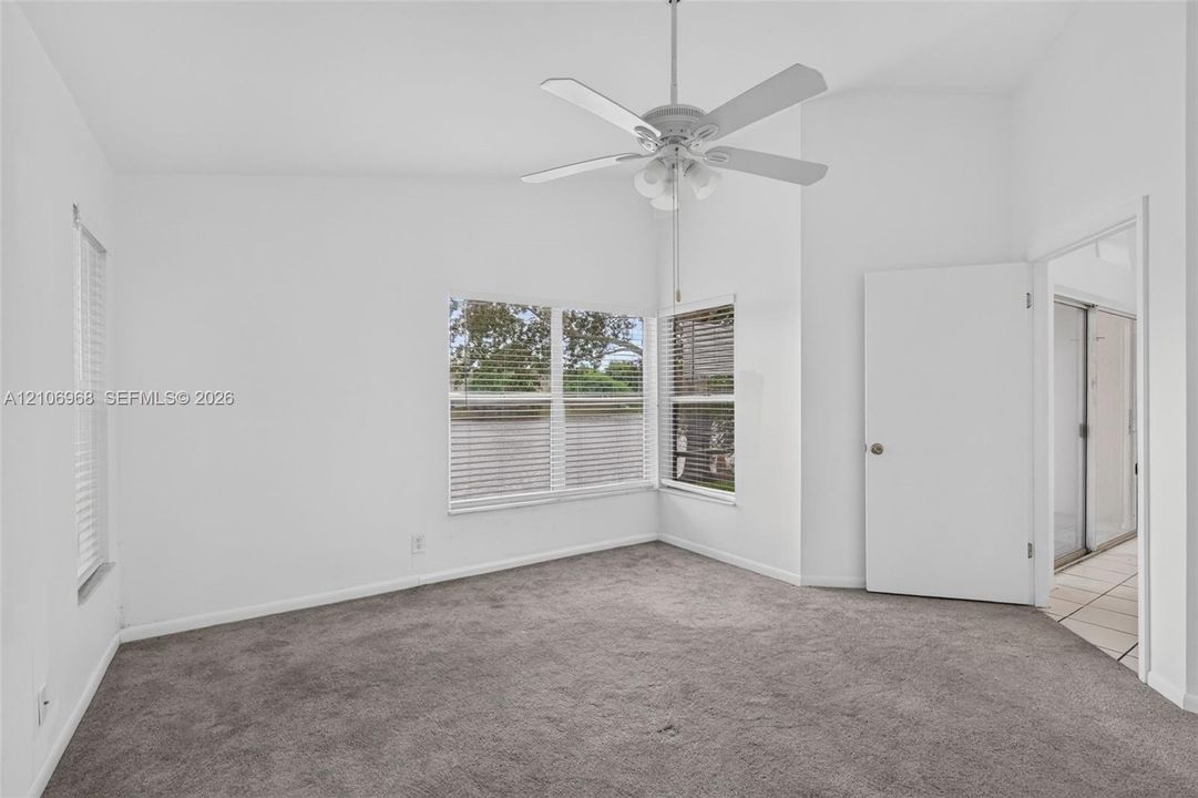 Vaulted ceilings featuring a white finish, neutral carpeting, multi-pane windows with horizontal blinds, and a central ceiling fan with integrated light fixture