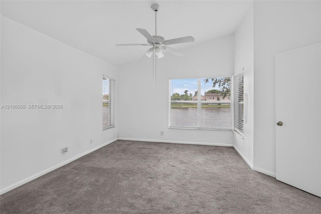 Room featuring vaulted ceilings, neutral carpeting, a white ceiling fan with integrated lighting, and dual-pane windows with water surroundings
