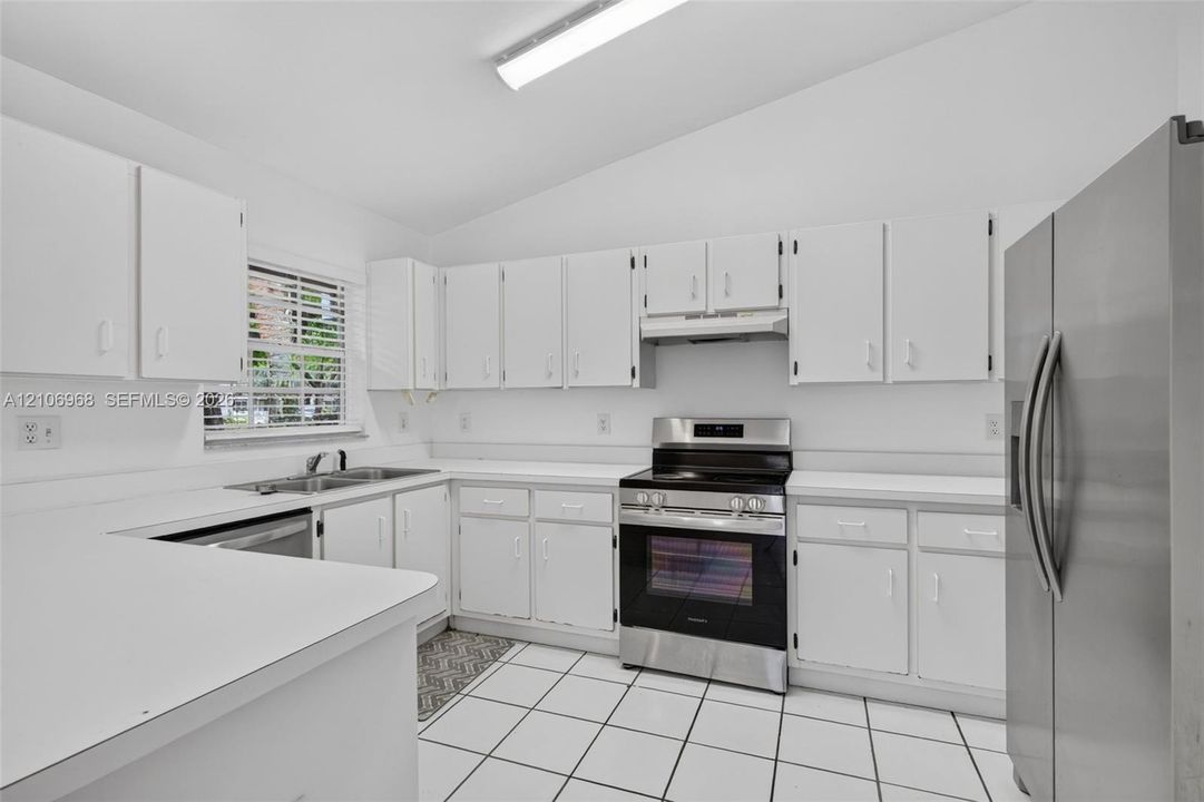 Kitchen featuring white cabinetry, stainless steel appliances, solid surface countertops, a dual-basin sink, and tiled flooring