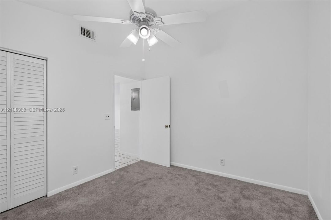 Interior room featuring neutral wall paint, wall-to-wall carpeting, white bi-fold closet doors, and a ceiling fan with integrated lighting