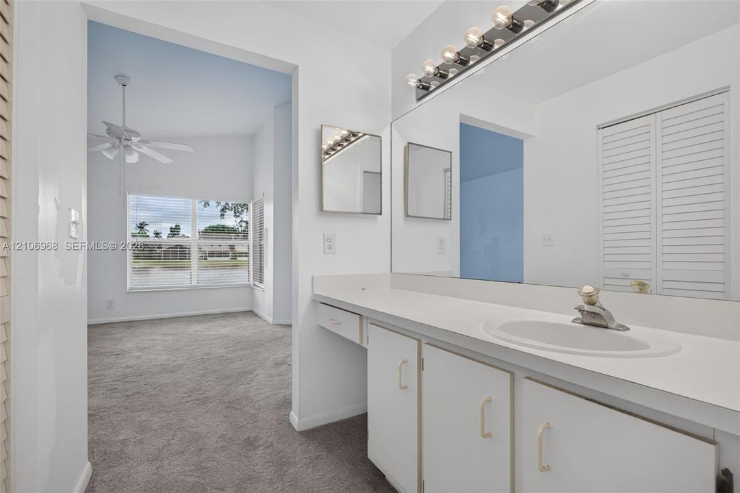 Bathroom featuring a full-width vanity mirror, integrated sink, and white cabinetry with a multi-bulb vanity light fixture
