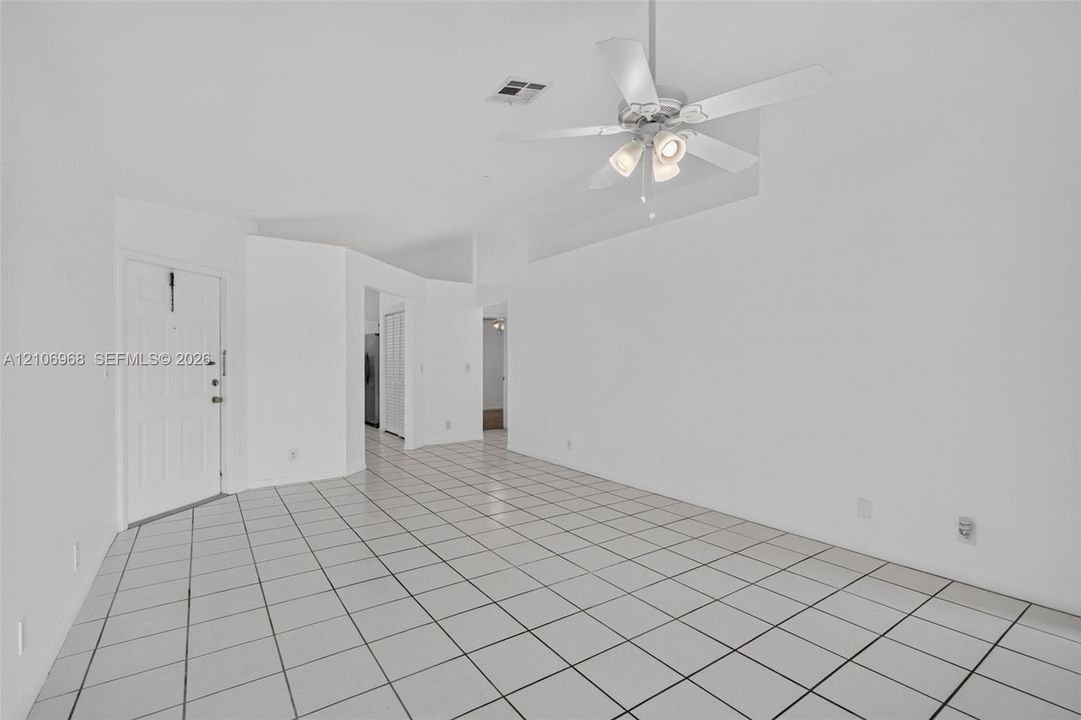 Open-concept interior featuring light-toned tile flooring, vaulted ceilings, and a ceiling fan with integrated lighting