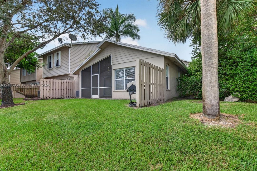 Exterior featuring horizontal siding, a screened-in lanai, wood-slat privacy fencing, and expansive grass lawn with mature trees
