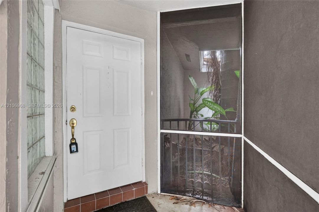 Entryway featuring a white six-panel door, glass block side window, ceramic tile threshold, and a screened enclosure with metal railings