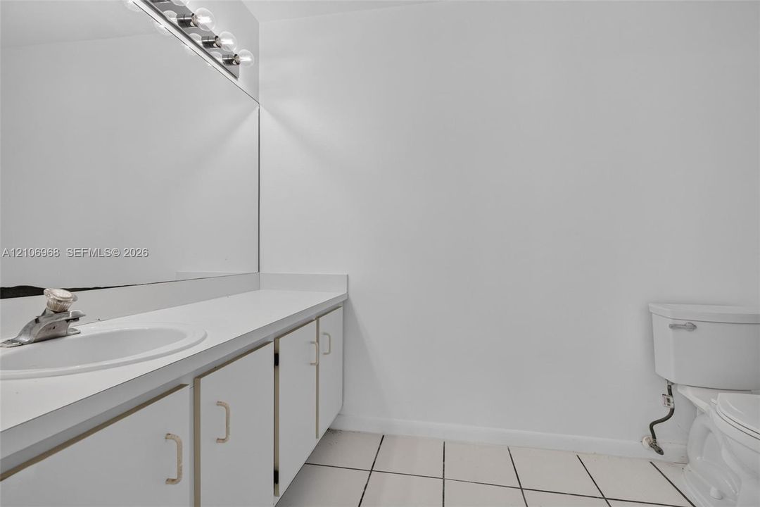 Bathroom featuring a vanity with integrated sink, expansive wall-mounted mirror, overhead vanity lighting, and ceramic tile flooring
