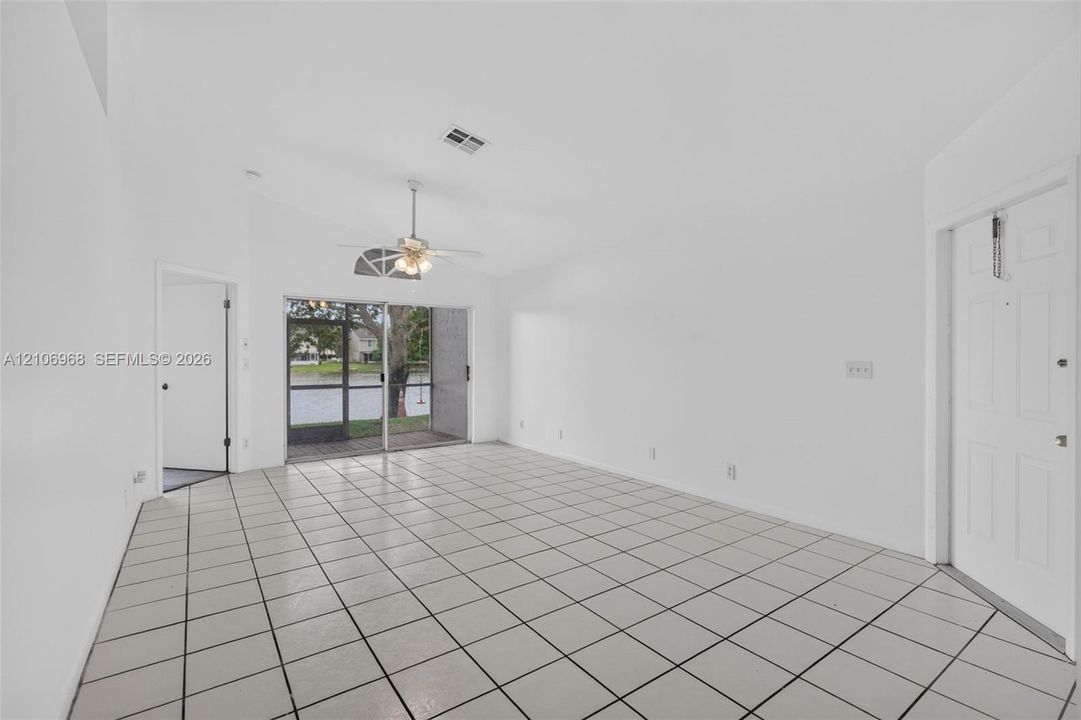 Vaulted ceilings, large-format ceramic tile flooring, ceiling fan with light fixture, and sliding glass doors with direct access to a screened-in lanai