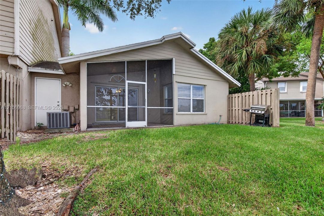 Rear exterior featuring a screened-in lanai, lap siding, and a fenced-in grassy yard with mature palm trees