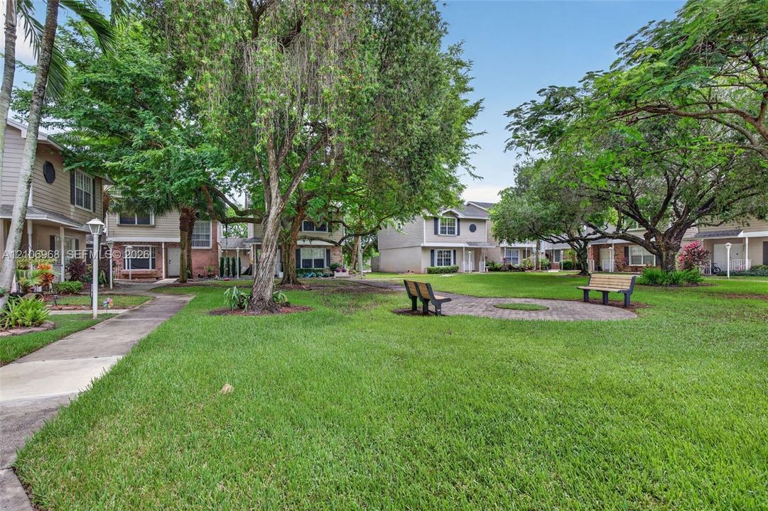 Common grounds featuring expansive lawn space, mature shade trees, paved walkways, and a circular stone-paver seating area