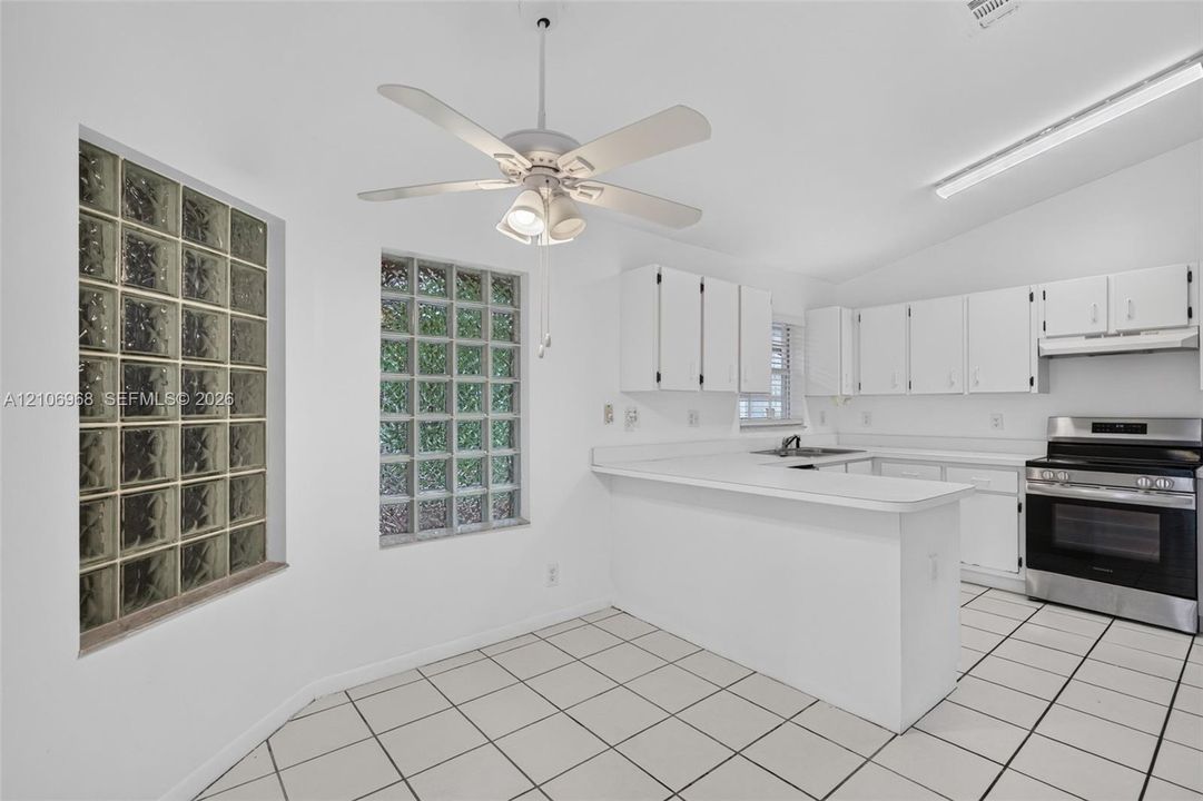 Kitchen featuring glass block windows, white cabinetry, a breakfast bar, ceramic tile flooring, and a stainless steel range