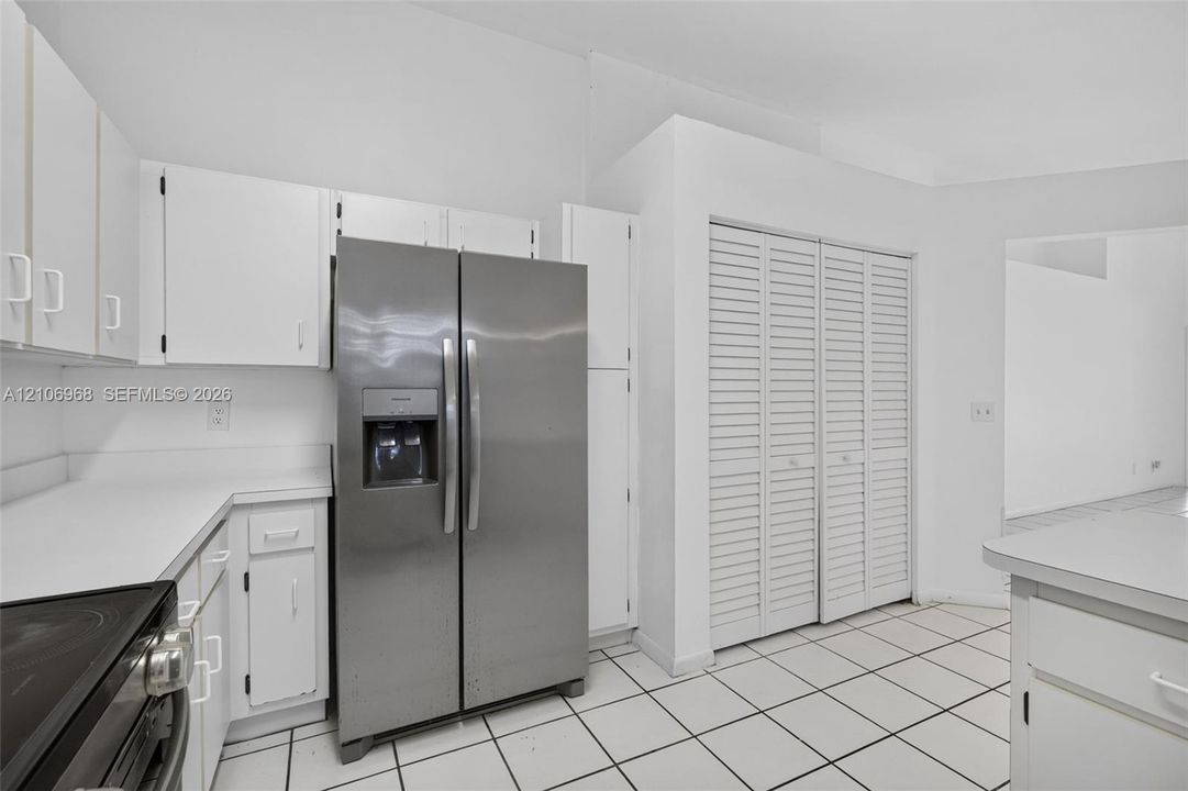 Kitchen featuring white cabinetry, integrated stainless steel side-by-side refrigerator, solid-surface countertops, tile flooring, and louvered closet doors