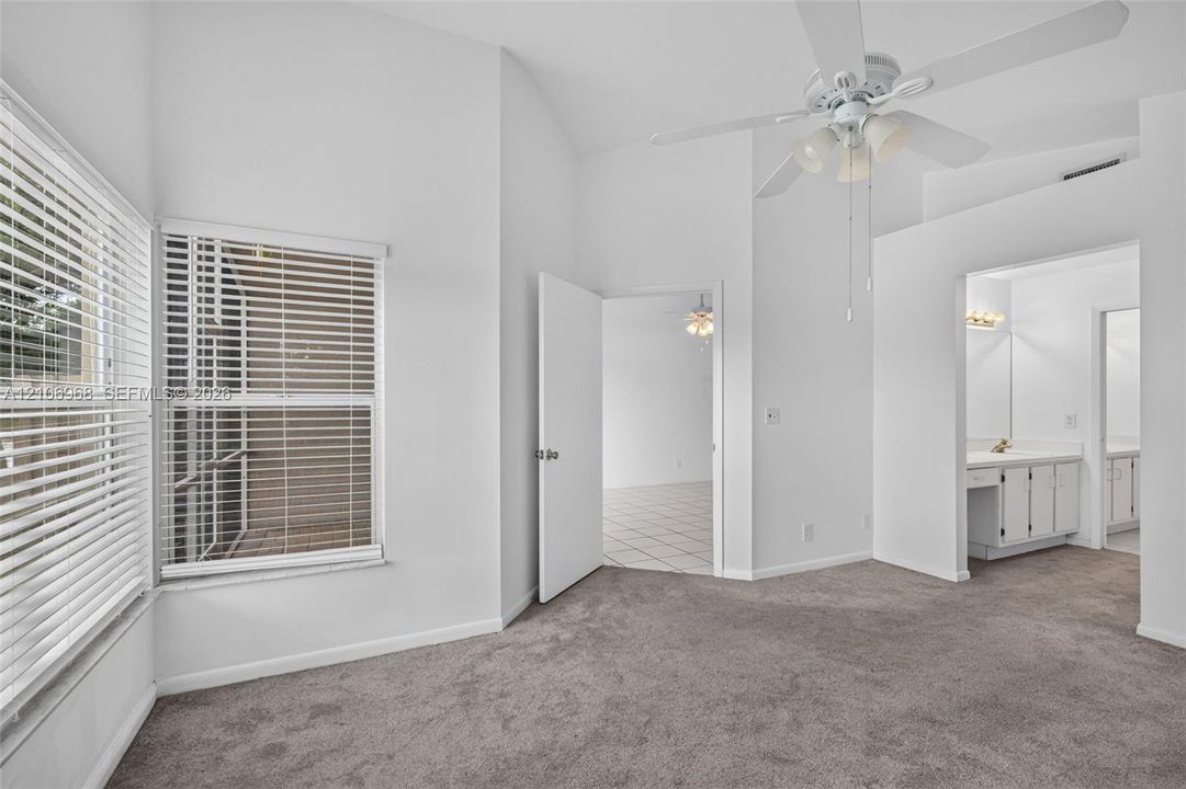 Room featuring vaulted ceilings, neutral carpeting, multi-light ceiling fan, and large windows with horizontal blinds