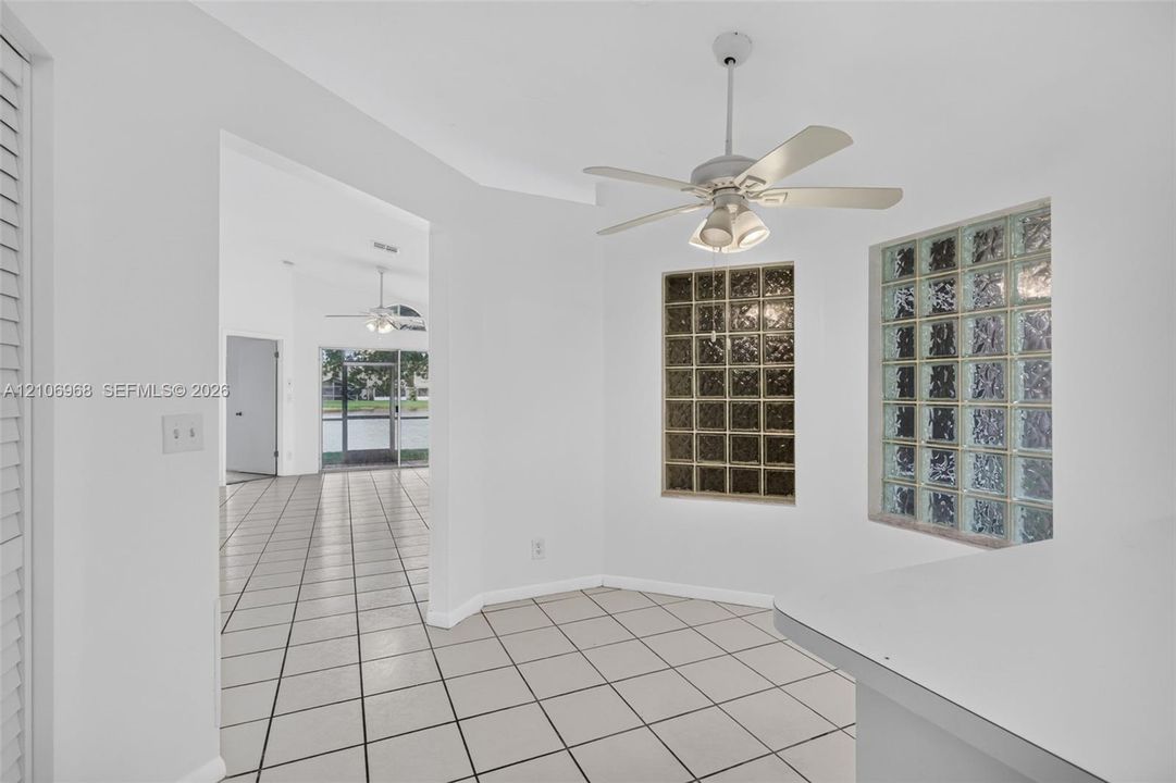 Interior area featuring large-format white tile flooring, white-painted walls, a ceiling fan with integrated lighting, and two textured glass block windows