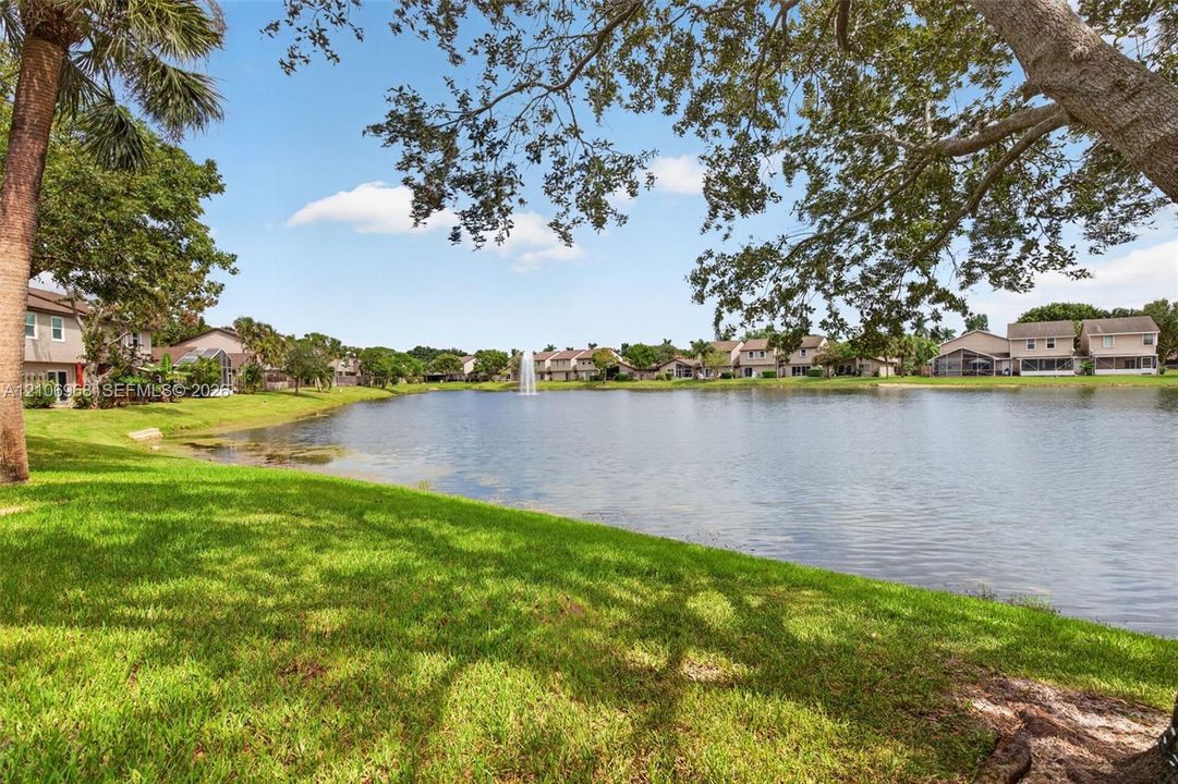 Waterfront grounds featuring a central fountain, manicured lawn, and mature canopy trees