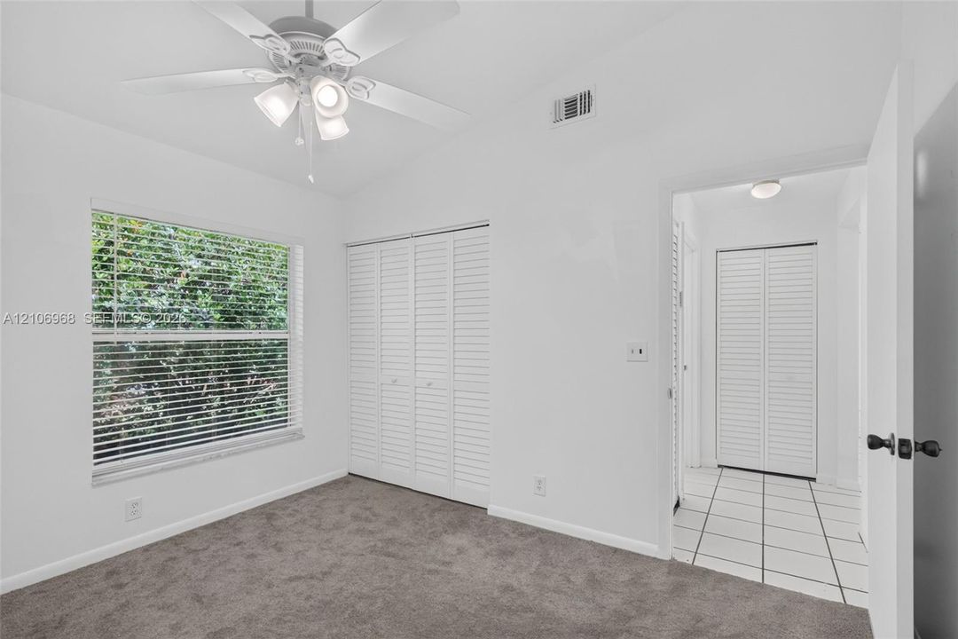 Room featuring wall-to-wall carpeting, vaulted ceiling with a white overhead fan, louvered bi-fold closet doors, and large dual-pane window with horizontal blinds