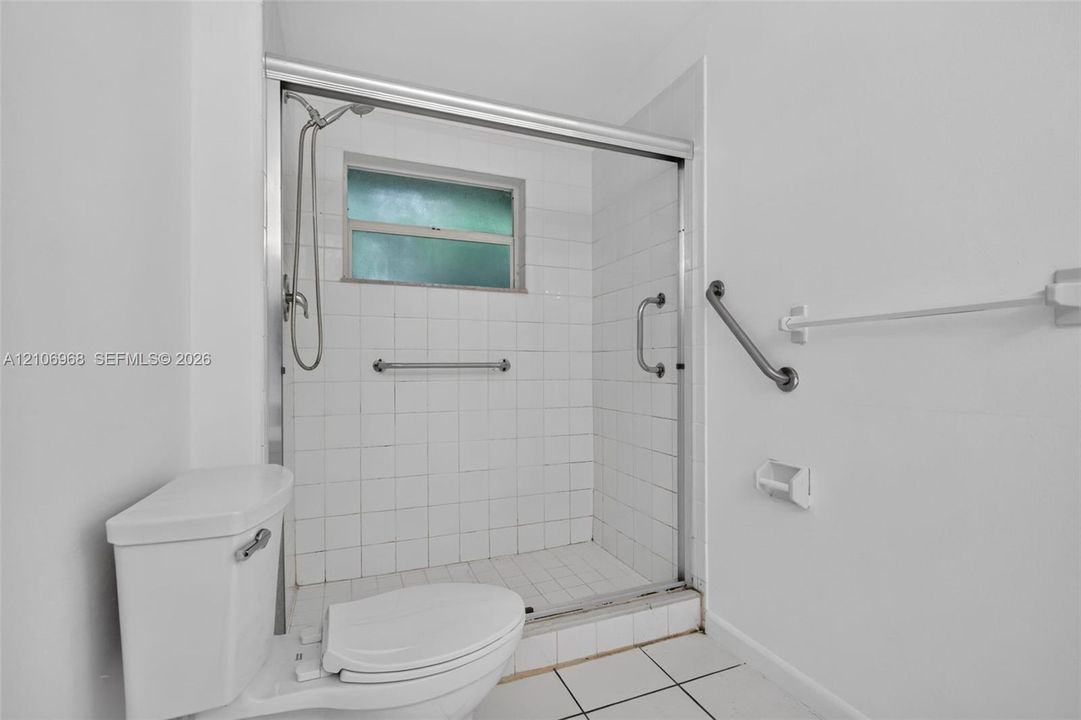 Shower stall featuring white wall tile, a framed glass enclosure, and a wall-mounted shower head