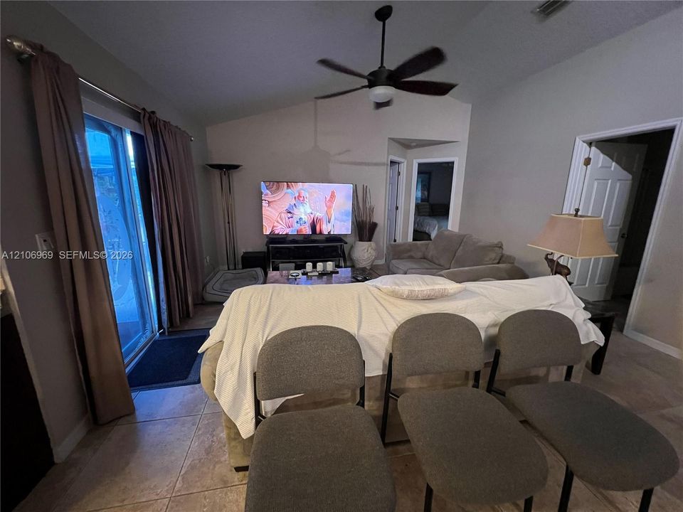 Living area featuring vaulted ceilings, tile flooring, a ceiling fan with integrated lighting, and a sliding glass door