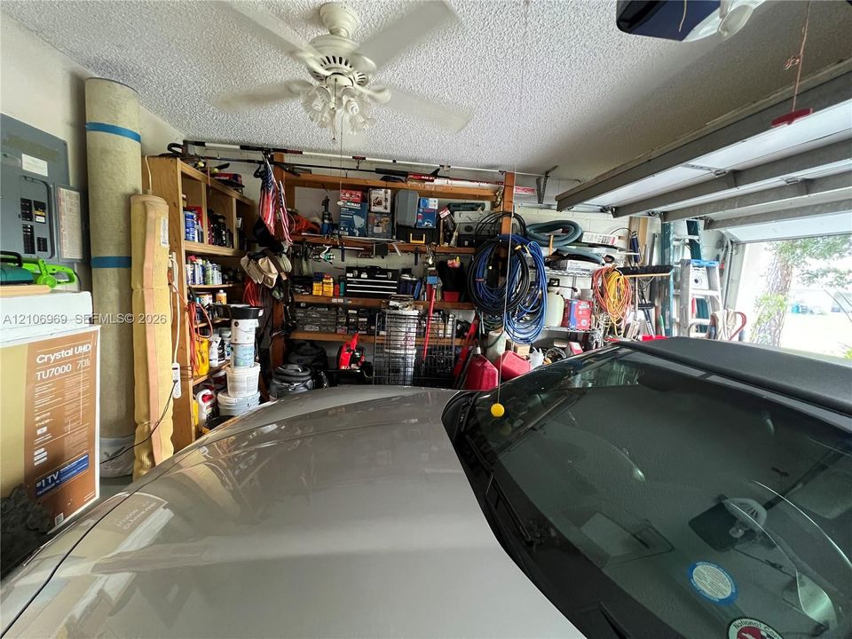 Attached garage featuring built-in wooden shelving, a ceiling-mounted fan, and an electrical service panel