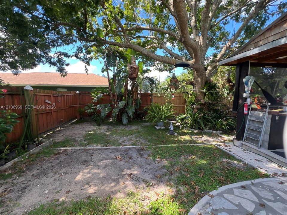 Rear yard featuring a wood fence, mature shade tree, stone-paver patio, and covered outdoor kitchen structure