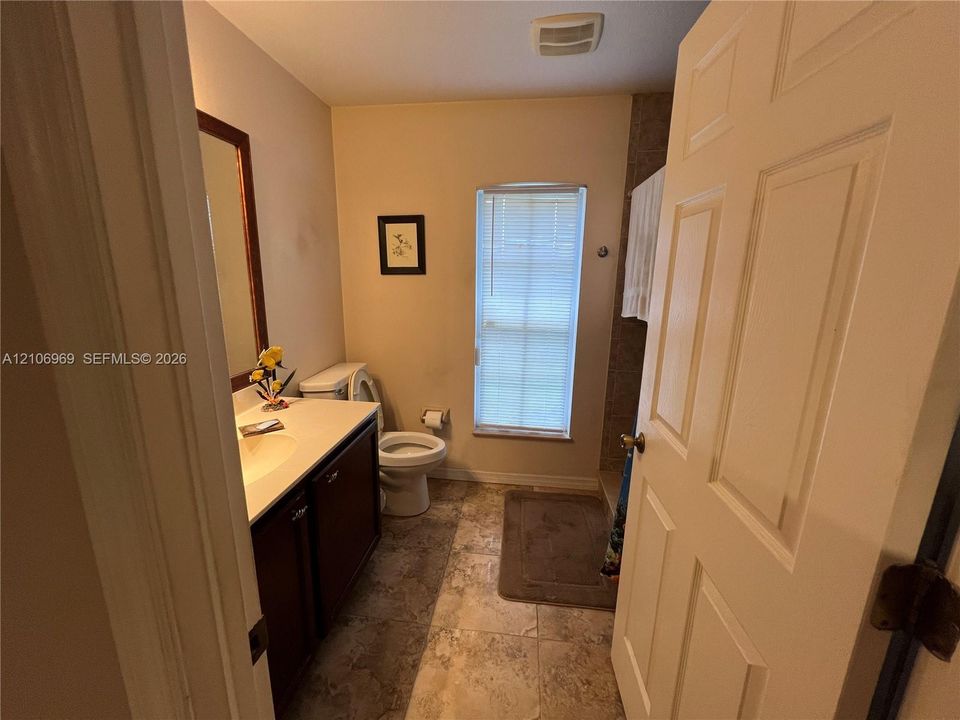 Bathroom featuring a vanity with a solid-surface countertop, tile flooring, and a window with integrated blinds