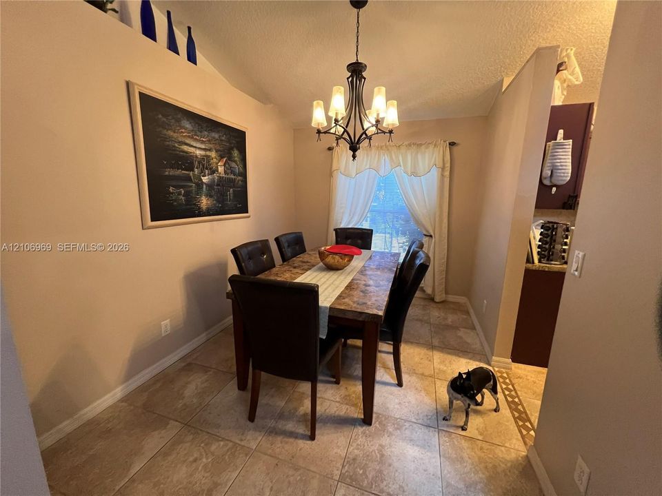 Dining area featuring neutral tile flooring, vaulted ceiling, and decorative iron-finish chandelier
