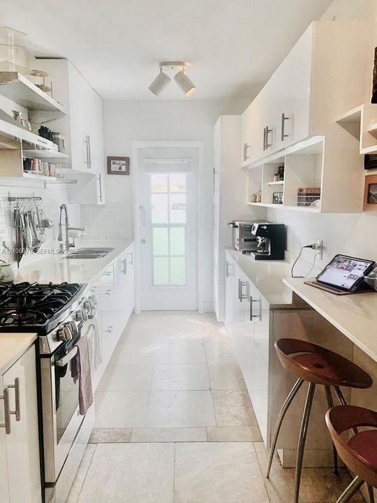Galley kitchen featuring high-gloss white cabinetry, stone-finish countertops, tile flooring, built-in open shelving, and a stainless steel gas range