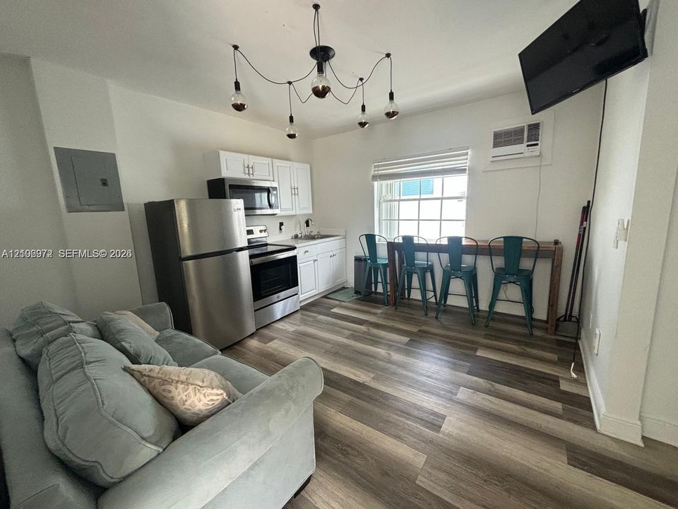 Kitchen area featuring white shaker-style cabinetry, stainless steel appliances, multi-toned wood-finish flooring, and a multi-arm industrial-style pendant light fixture