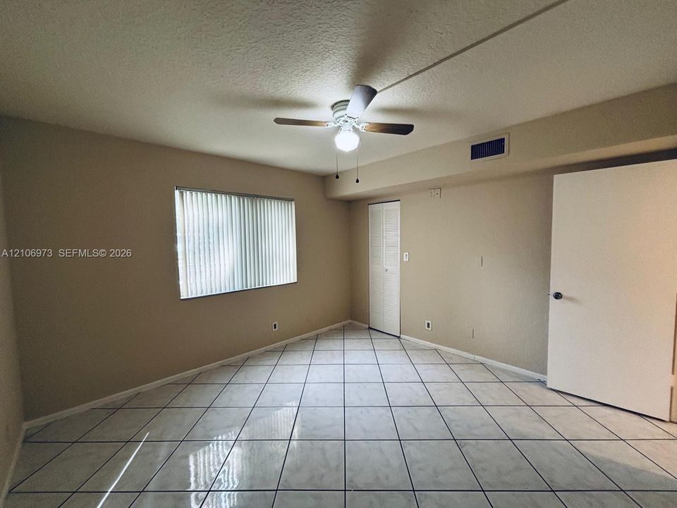 Room featuring neutral wall paint, tile flooring, ceiling fan with integrated light fixture, vertical window blinds, and a louvered-panel closet door