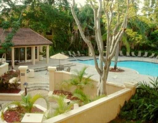 Community pool area featuring an in-ground swimming pool, tiered concrete decking, masonry perimeter wall, covered pavilion, and mature landscaping
