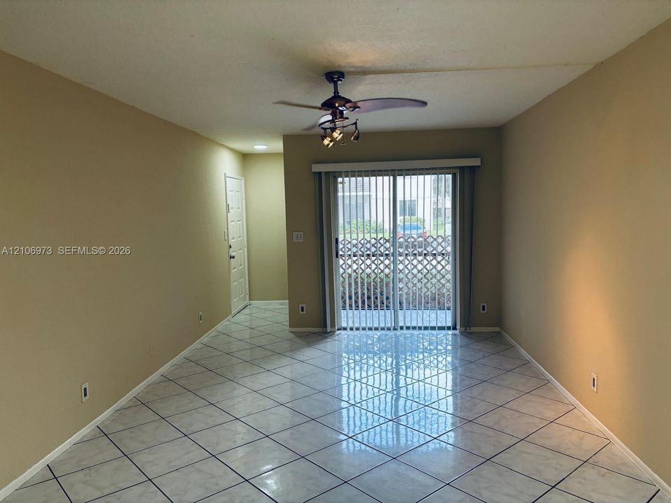 Neutral-toned interior featuring large-format tile flooring laid on a diagonal, sliding glass patio door, and a ceiling fan with multi-light fixture