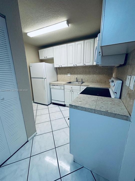 Kitchen featuring white cabinetry, tiled countertops, a double-basin stainless steel sink, ceramic tile flooring, and integrated white appliances