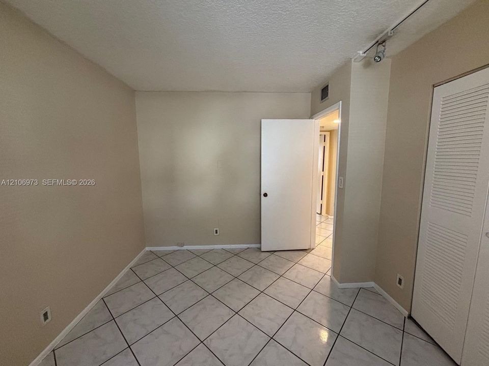 Interior room featuring large-format diagonal tile flooring, built-in louvered closet doors, and adjustable track lighting