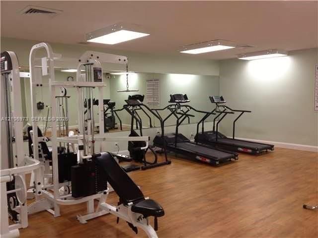 Fitness room featuring wood-finish flooring, wall-to-wall mirrors, and flush-mount lighting fixtures