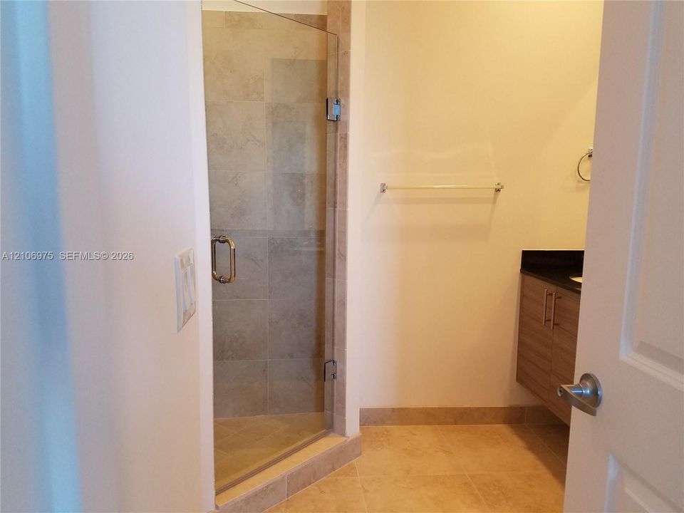 Shower featuring a glass door and neutral-toned wall tiling, accompanied by a vanity with dark countertop and wood-finish cabinetry
